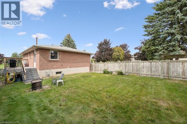 Another view of the backyard showing grass, fence, and a fire pit. - 121 Nathaniel Crescent, Kitchener