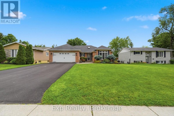 View of the bungalow's driveway leading to the white garage door, with green grass on both sides. - 121 Simcoe Street, Greater Napanee