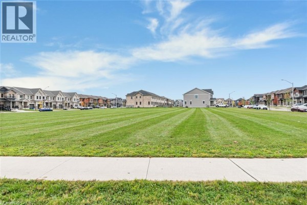 Expansive view of a freshly cut, empty green field with houses lining the distant street. - 121 Vanilla Trail, Thorold
