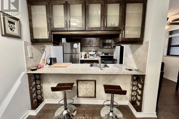 Kitchen with a breakfast bar, two stools, and wood cabinets above granite countertops. - 1210 - 120 Saint Patrick Street N, Toronto