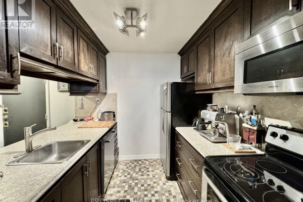 Narrow kitchen with stainless steel appliances, granite countertops, and dark wood cabinets. - 1210 - 120 Saint Patrick Street N, Toronto