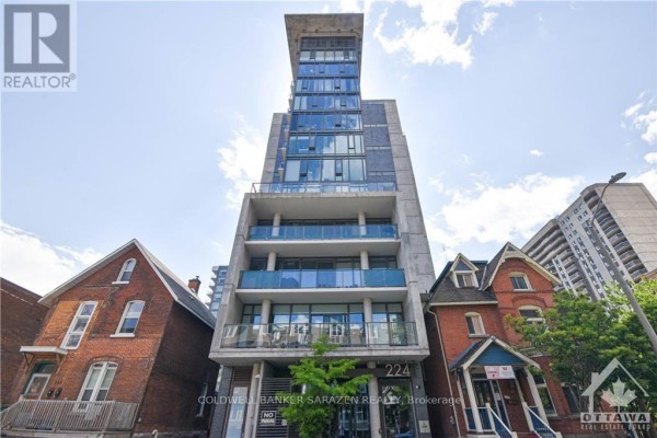 Front exterior of a tall, modern apartment building with glass panels and blue railings on balconies. - 1210 - 224 Lyon Street, Ottawa