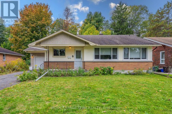 Exterior of the house with a green lawn, driveway, and trees in the background. - 1210 Adirondack Drive, Ottawa