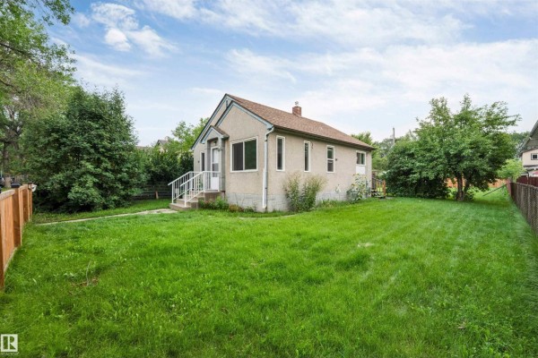 Rear exterior of the house showcasing the large backyard with green grass and mature trees. - 12105 87 St Nw, Edmonton