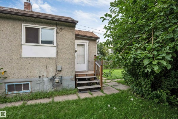 Close-up of the back door and exterior of the house, showing concrete steps and a small basement window. - 12105 87 St Nw, Edmonton