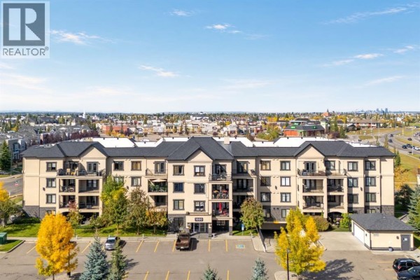Aerial view of a beige apartment building with a black roof and surrounding trees and parking lot. - 1211, 310 Mckenzie Towne Gate Se, Calgary