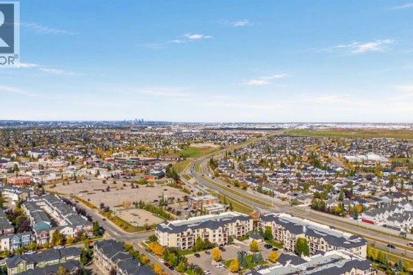 Aerial view of a suburban neighborhood with a highway, residential buildings, and distant city skyline. - 1211, 310 Mckenzie Towne Gate Se, Calgary