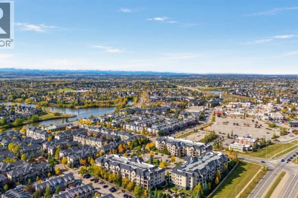 Aerial view of a suburban neighborhood with a lake, residential buildings, and distant mountains on the horizon. - 1211, 310 Mckenzie Towne Gate Se, Calgary