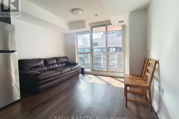 A living area with a brown leather sofa, two wooden chairs, and a sliding glass door. - 1211 - 3091 Dufferin Street, Toronto