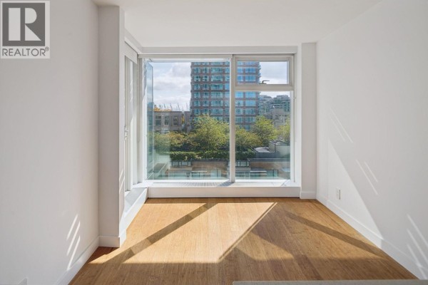 Interior room with light wood floors, white walls, and a large window showing city buildings. - 1211 777 Richards Street, Vancouver