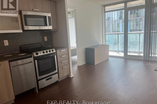 Apartment kitchen with stainless steel appliances, dark counters, and wooden floors. - 1212 - 36 Lisgar Street, Toronto