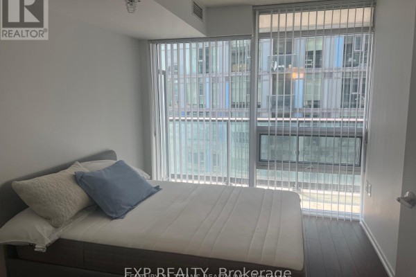 Bedroom with a bed, blue pillows, and floor-to-ceiling windows with vertical blinds. - 1212 - 36 Lisgar Street, Toronto