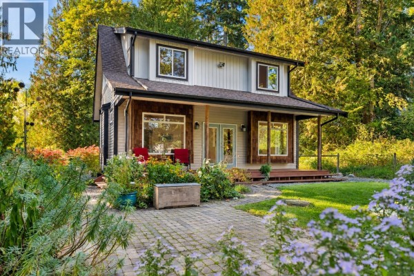 Side view of a two-story house with wood siding accents and a colorful garden. - 12121 264 Street, Maple Ridge