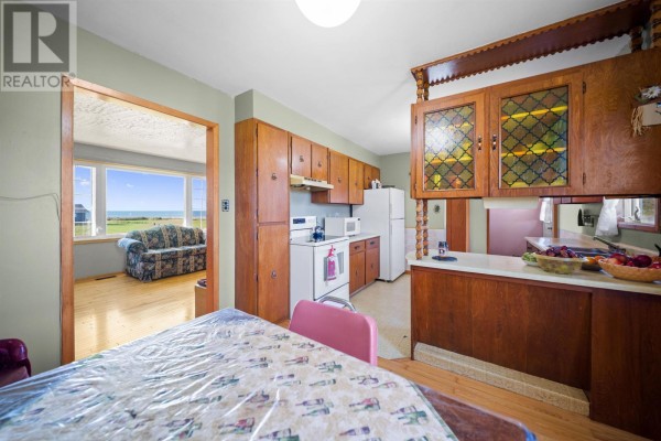 Kitchen with light green walls, wood cabinets, white appliances, and a view of the living room and ocean. - 12122 Rte 14, Pleasant View