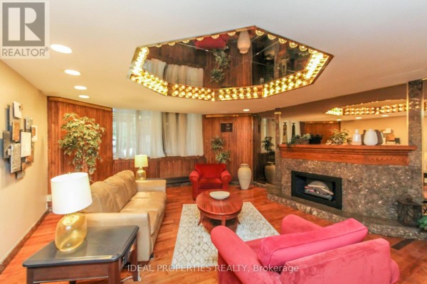 Living room area with two sofas, a coffee table, fireplace, mirrored ceiling, and wood-paneled walls. - 1213 - 2871 Richmond Road W, Ottawa
