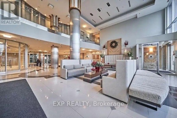 A view of the condo lobby with white seating, glass elevators, and decorative accents. - 1213 - 58 Marine Parade Drive, Toronto