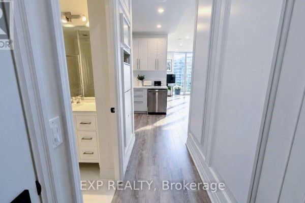 Hallway view showing a white bathroom with double vanity and modern kitchen area. - 1213 - 58 Marine Parade Drive, Toronto