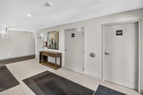 Apartment building hallway with beige tile floors, several doors, and wall art. - 1213 65 Fiorentino Street, Winnipeg