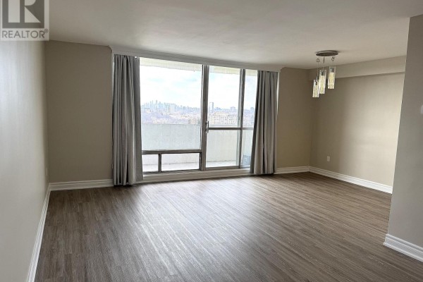 Empty living room with large windows, light beige walls, and dark wood laminate flooring. - 1214 - 1 Massey Square, Toronto