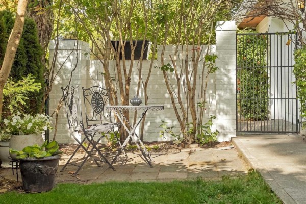 Small metal table and chairs set on a paved patio surrounded by lush greenery. - 12141 Sullivan Street, Surrey