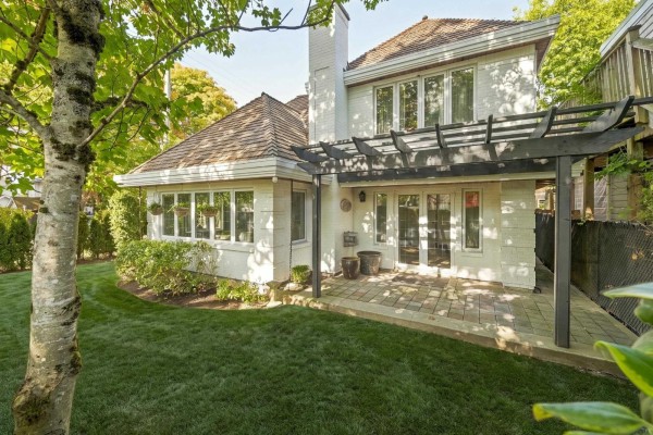Backyard view of a white house with a covered patio, stone pavers, and a manicured lawn. - 12141 Sullivan Street, Surrey