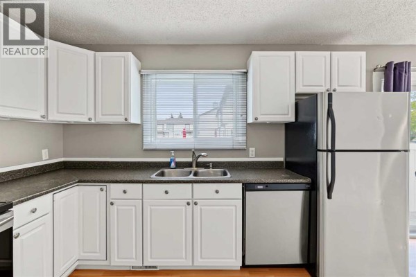 Kitchen with white cabinets, stainless steel refrigerator, and dishwasher. - 1215 137 Avenue Se, Calgary