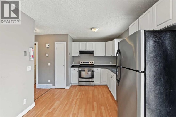 View of the kitchen from the hallway, showing white cabinets and appliances. - 1215 137 Avenue Se, Calgary