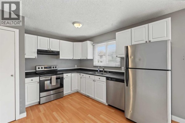 Kitchen corner with stainless steel refrigerator, white cabinets, and window. - 1215 137 Avenue Se, Calgary