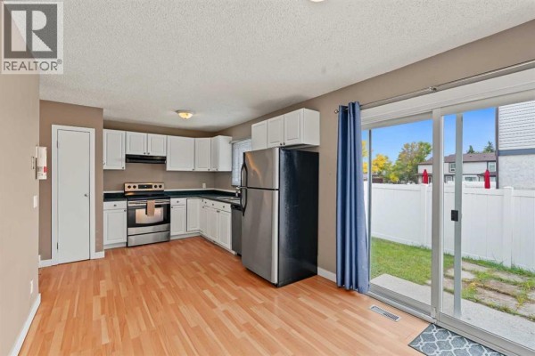 Kitchen with white cabinets, stainless steel refrigerator, and sliding door to backyard. - 1215 137 Avenue Se, Calgary