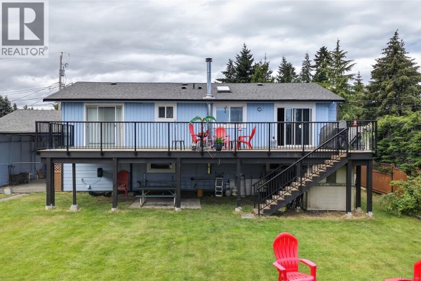 Close-up of the light blue house entrance with a Canadian flag and flowering bushes. - 1215 Gilley Cres, Parksville