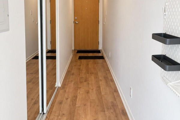 Hallway with a sliding mirrored closet door, wooden floor, and a closed light brown door. - 1216 - 38 Joe Shuster Way, Toronto