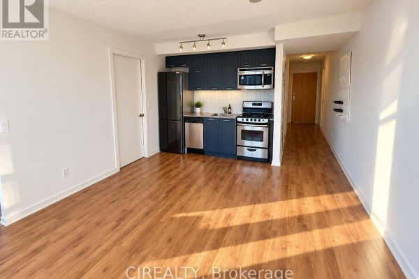 Open-concept living area with a kitchen featuring dark blue cabinets, stainless steel appliances, and hardwood floors. - 1216 - 38 Joe Shuster Way, Toronto