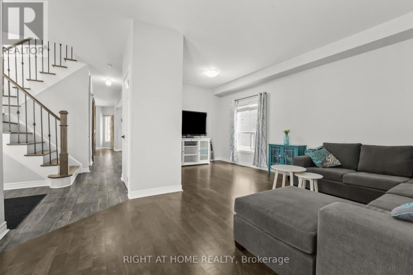 Living room with a gray sectional sofa, blue cabinet, coffee tables, and a view of the staircase. - 1216 Fox Hill Street, Innisfil