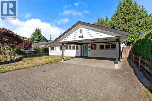 Exterior view of a white bungalow with a paved driveway and landscaping. - 1216 Pinewood Crescent, North Vancouver