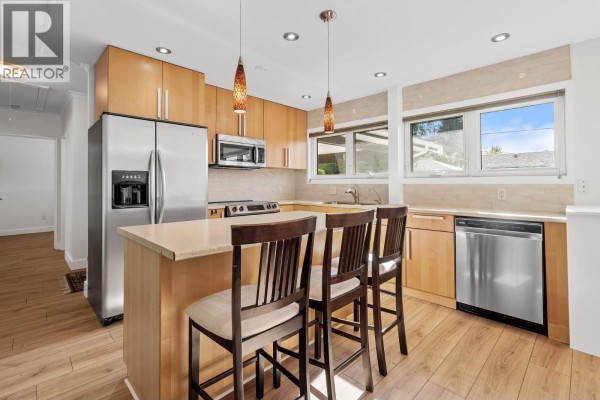 Kitchen with light wood cabinets, stainless steel appliances, and a central island. - 1216 Pinewood Crescent, North Vancouver