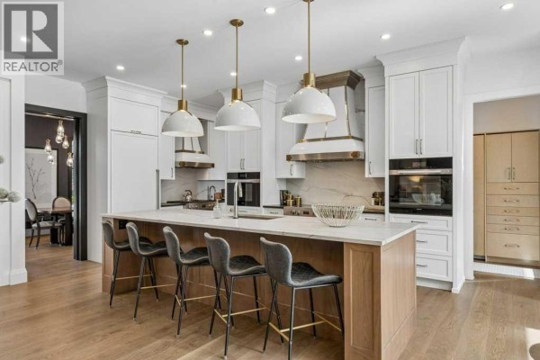 Spacious kitchen with a large island, white cabinetry, stainless steel appliances, and light wood flooring. - 1217 38 Avenue Sw, Calgary