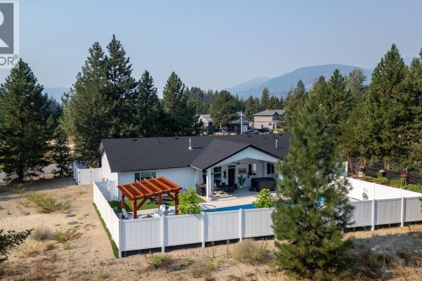 Rear exterior of the white house, showing the pool, fenced yard, and mountain backdrop. - 1217 Mcphee Road, Castlegar