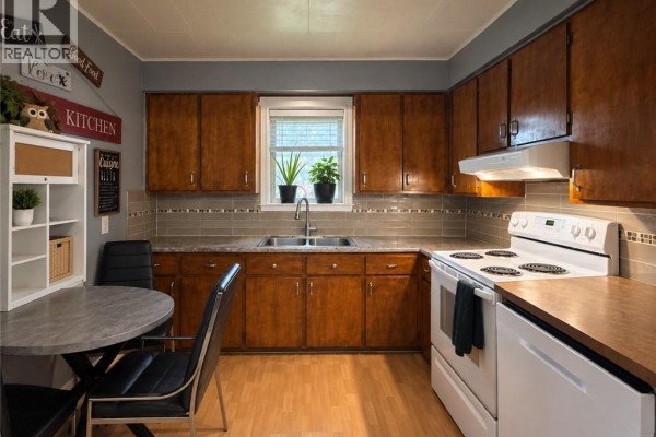 Kitchen with light wood cabinets, grey tiled backsplash, stainless steel sink, and white appliances. - 1219 St-francois Street, Verret