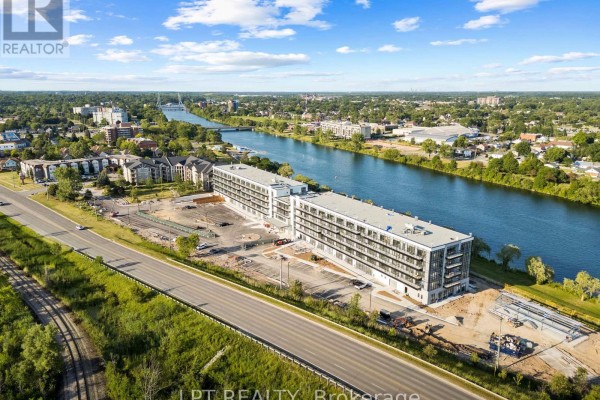 Aerial view of apartment buildings along a wide river, with a highway and residential areas visible. - 122 - 350 Prince Charles Drive S, Welland