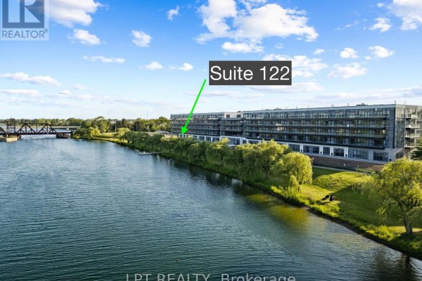 Exterior view of modern apartment buildings with balconies alongside a large river on a sunny day. - 122 - 350 Prince Charles Drive S, Welland