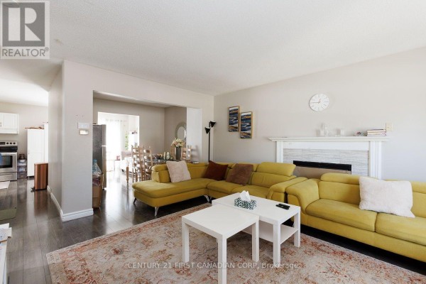 Open concept living room with a yellow sectional sofa, fireplace, and view into the dining area and kitchen. - 122 - 70 Fiddlers Green Road, London North