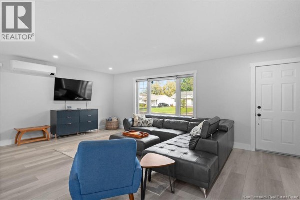 Living room with a dark grey sectional sofa, blue armchair, television, and light wood floors. - 122 Dolbeau Street, Dieppe