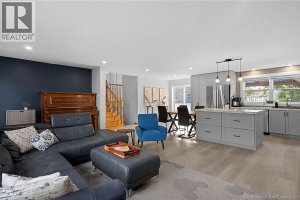 Open-concept living area featuring a sectional sofa, dining table, kitchen island, and grey cabinets. - 122 Dolbeau Street, Dieppe