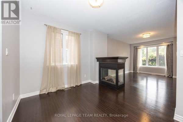 Living room with dark hardwood floors, a dark fireplace surround, and large windows with beige curtains. - 122 Highbury Park Drive S, Ottawa