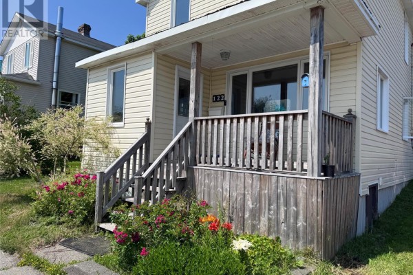 Close-up of the wooden porch stairs and railing with blooming pink flowers. - 122 Lincoln Road, Grand Falls Windsor