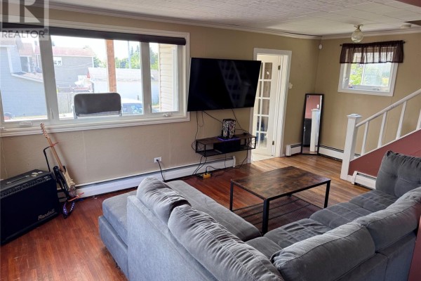 Living room with a large TV, sectional sofa, coffee table, and hardwood floors. - 122 Lincoln Road, Grand Falls Windsor