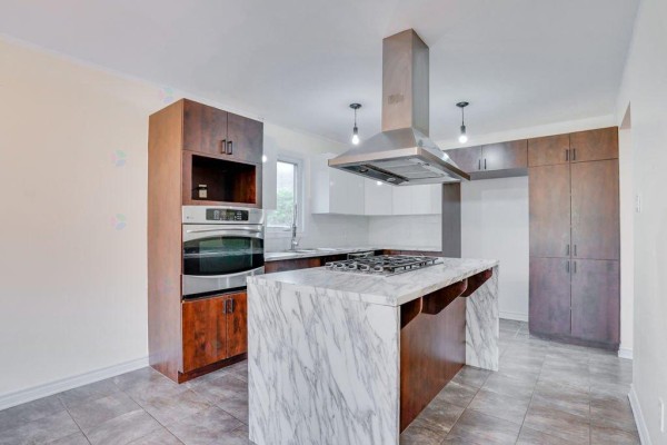 Modern kitchen with marble island, stainless steel appliances, and dark wood cabinets. - 122 Rue Du Totem, Gatineau