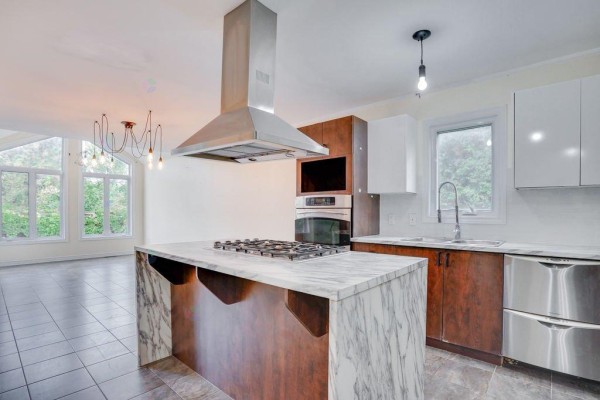 Spacious kitchen with island, overlooking a living area with large windows and vaulted ceiling. - 122 Rue Du Totem, Gatineau