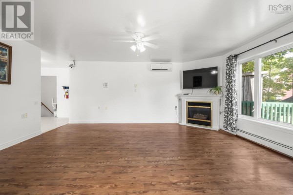 Living room with hardwood floors, a white fireplace, large window, and a mounted television. - 122 Victoria Street, Windsor