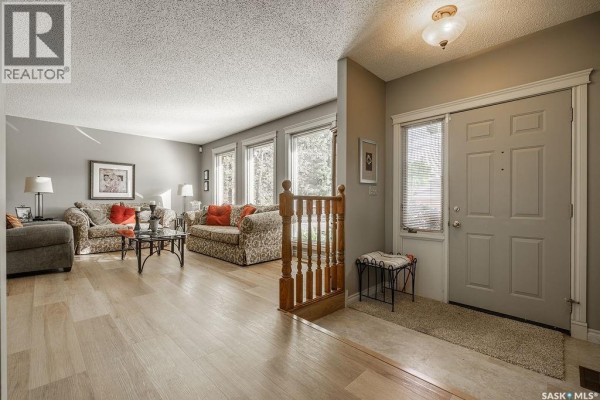 Living room with a fireplace, large windows, and light wood floors. - 122 Wakaw Crescent, Saskatoon